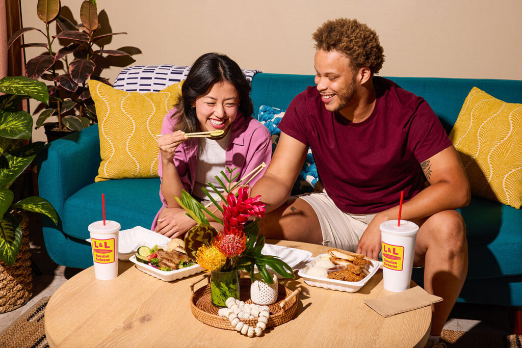 Man and Woman share a meal seated on a couch.